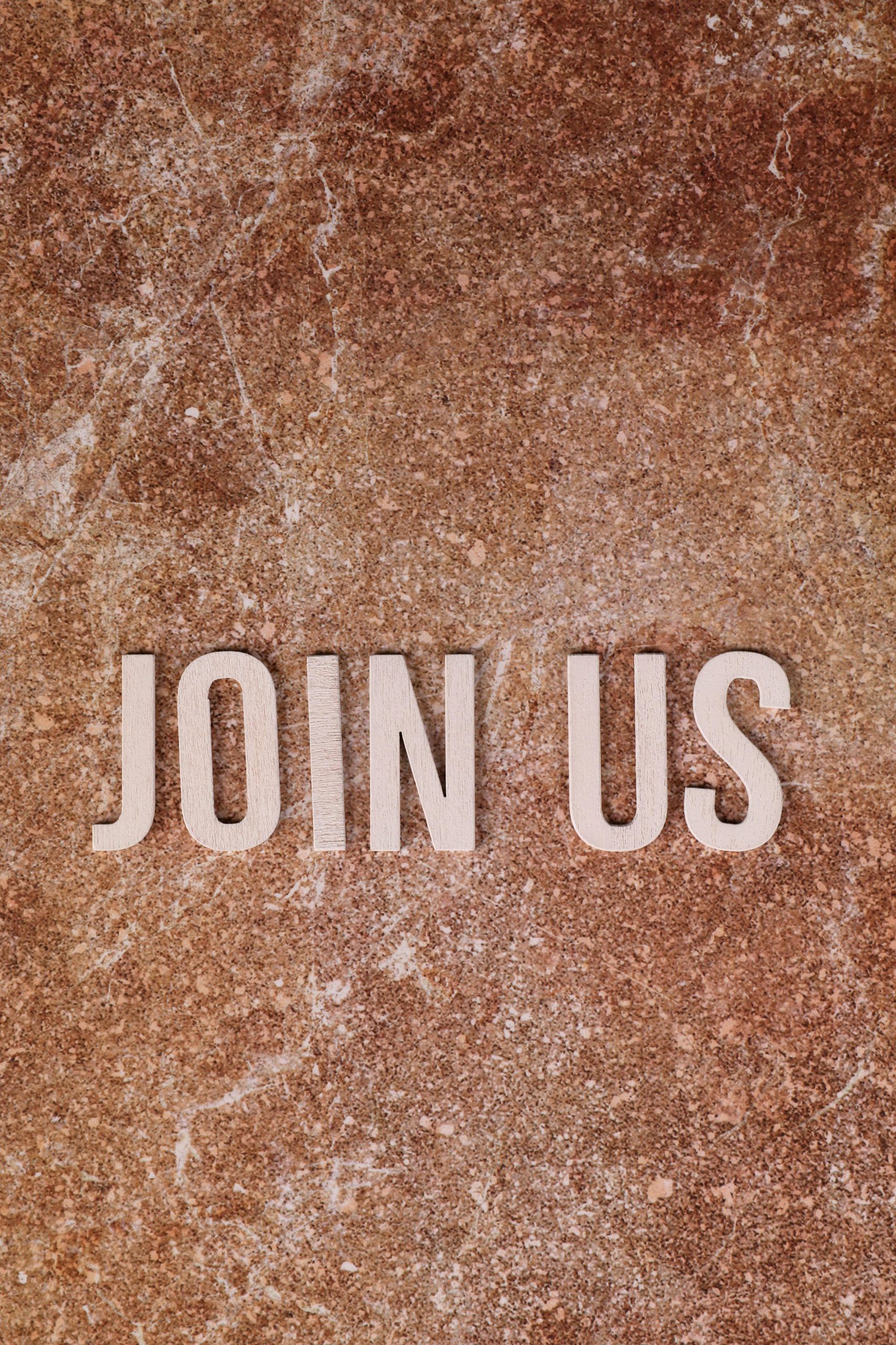 Flat lay of 'Join Us' text on a rustic stone background, inviting participation.